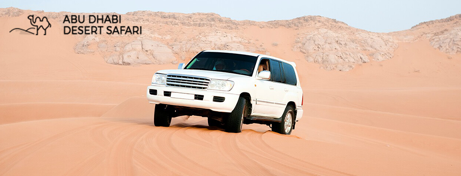 A car driving on desert dunes with rocky backdrop during an Abu Dhabi Desert Safari.